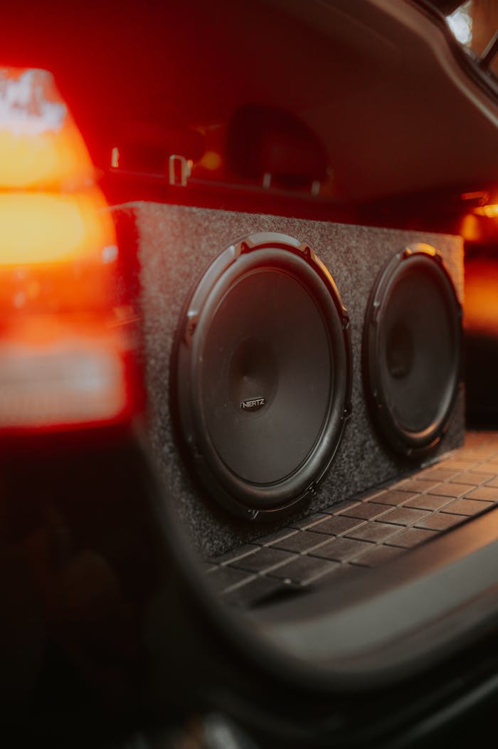 Close-up of dual subwoofers in a car trunk with glowing lights.